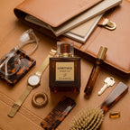 Sabotage Amber Oud Eau de Parfum bottle and travel spray in a warm leather flat-lay arrangement with grooming accessories, watch, and eyeglasses.